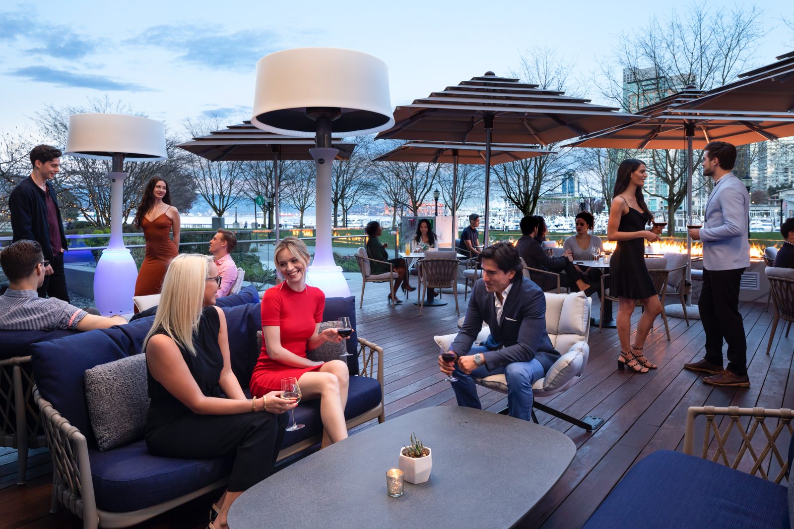 Guests mingling on a rooftop lounge at dusk beside a color-changing Kindle lamp