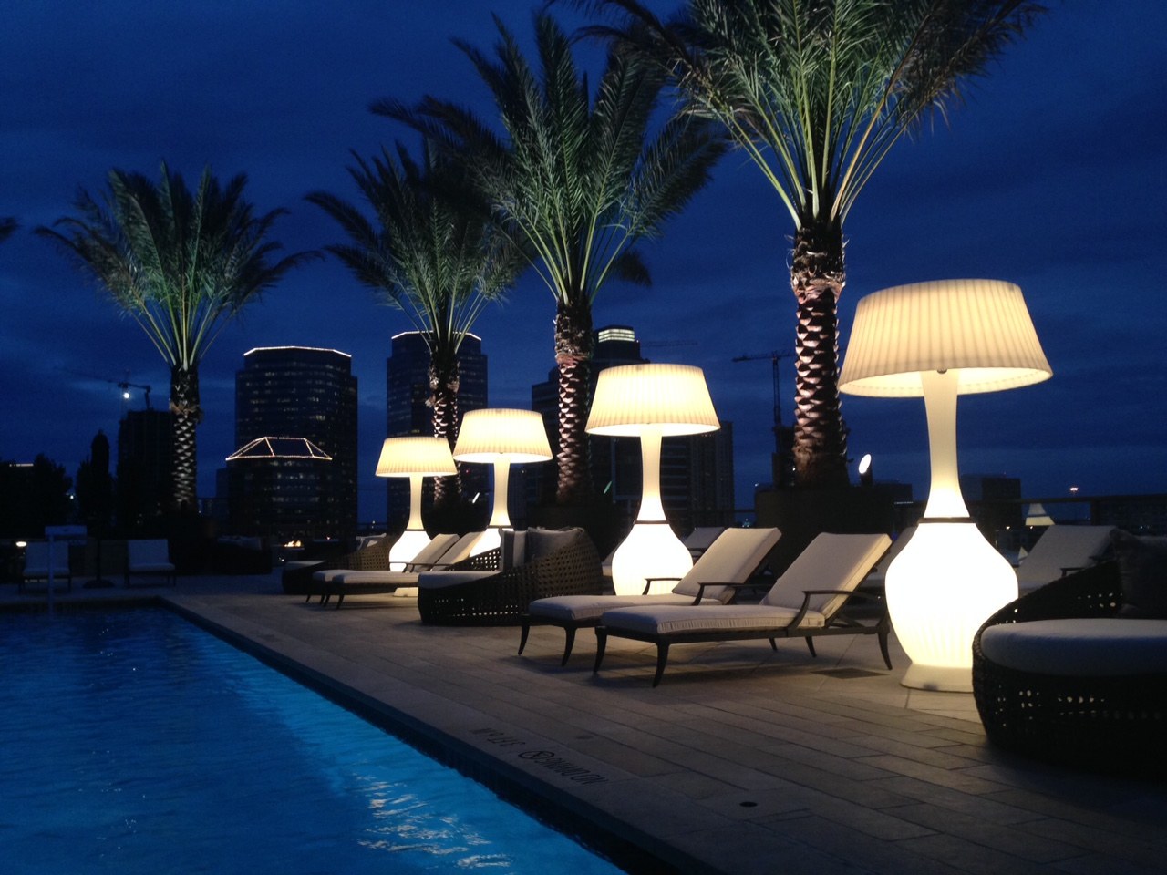 Kindle lamps glowing beside a rooftop pool with the city skyline at night